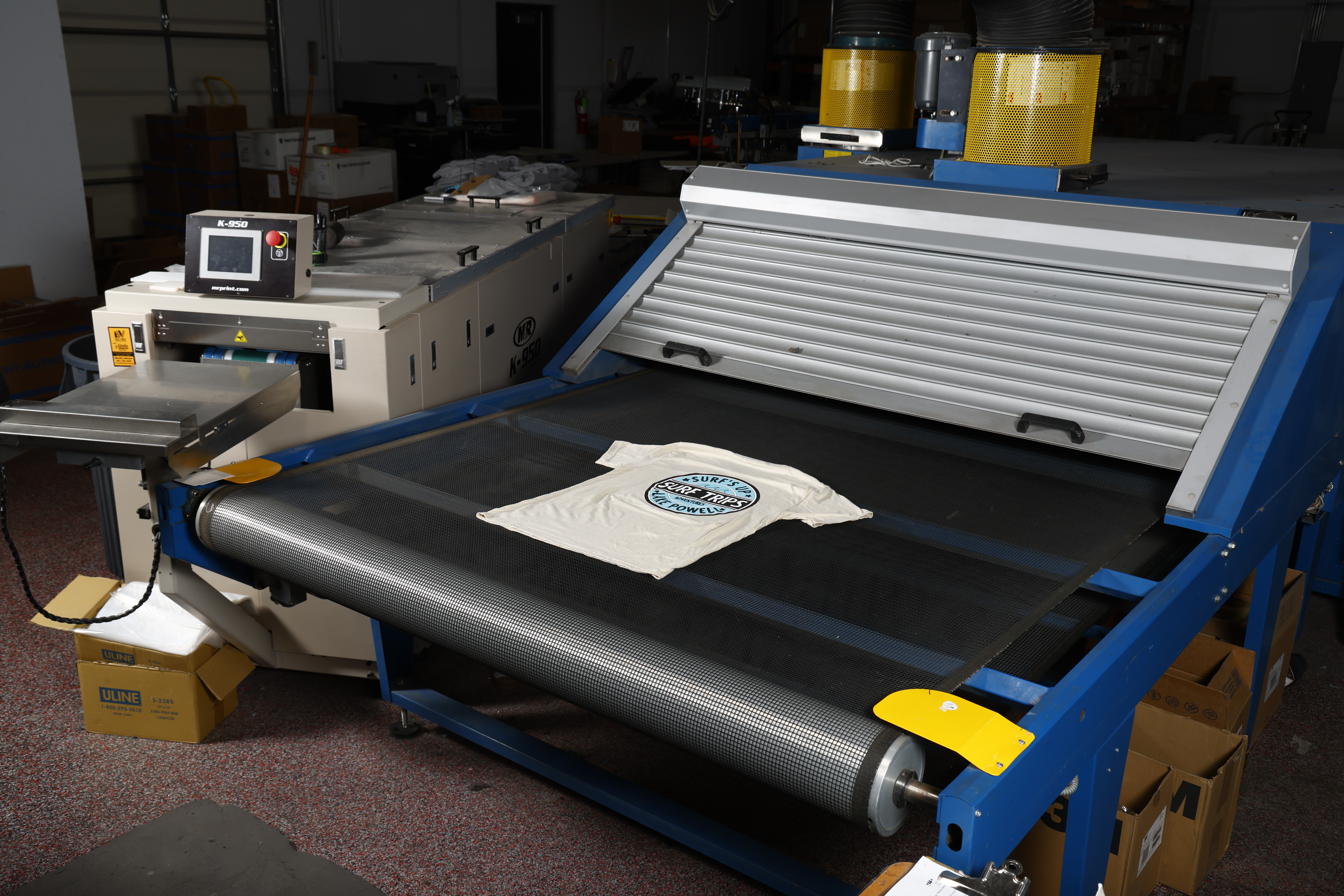 A picture of a surf shop t-shirt being printed on a screen printing machine.